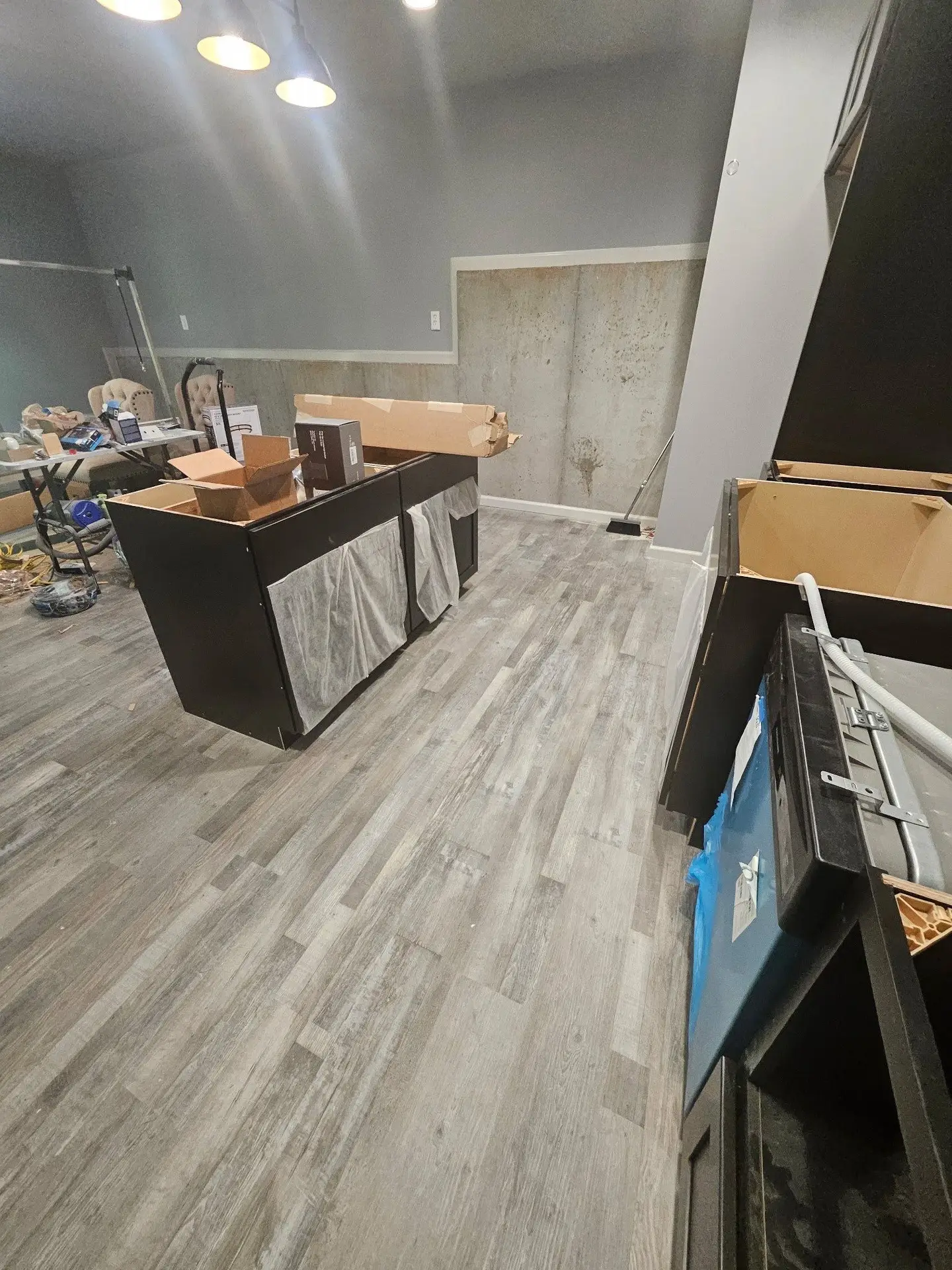 Bare concrete floor and unfinished framing of a basement area designated for a new kitchen installation.